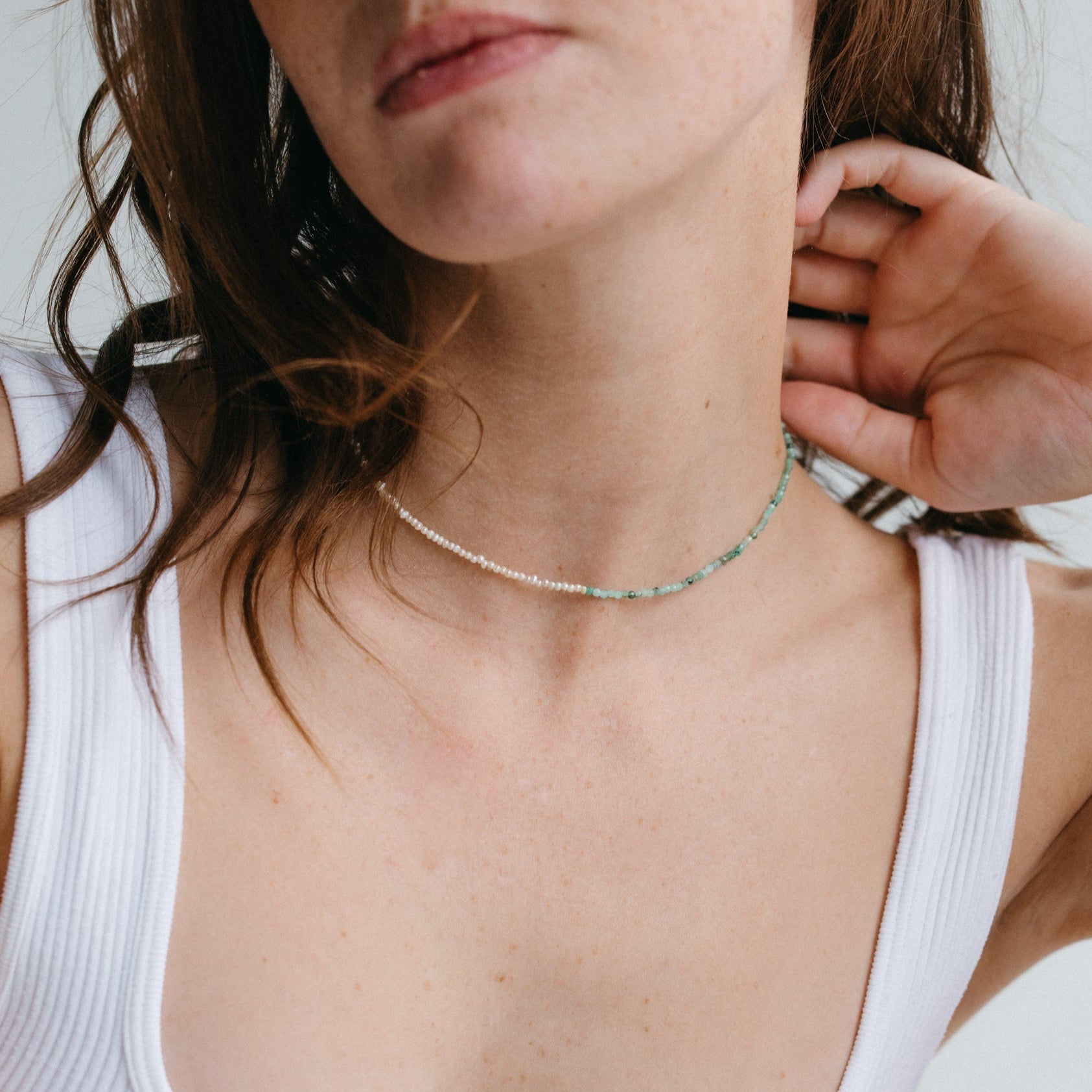 Femme portant le collier Emmie en perles de culture et pierres émeraude, bijou raffiné fait main, porté sur peau nue avec débardeur blanc, idée cadeau femme.